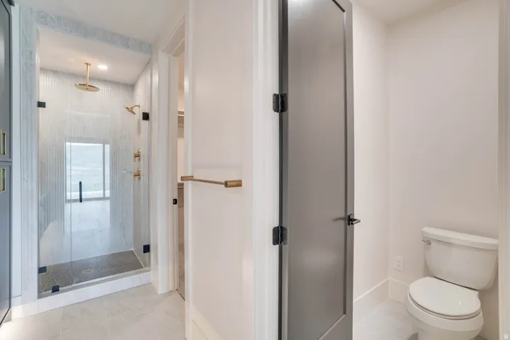 Spacious shower enclosure with clear glass door, gold-finish fixtures including rain showerhead, and tiled walls