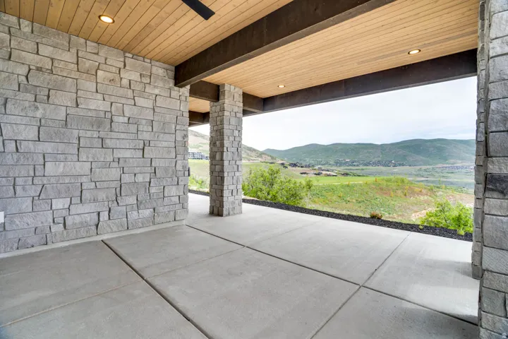 Expansive covered patio featuring concrete flooring, stone veneer walls and columns, and a wood-paneled ceiling with recessed lighting
