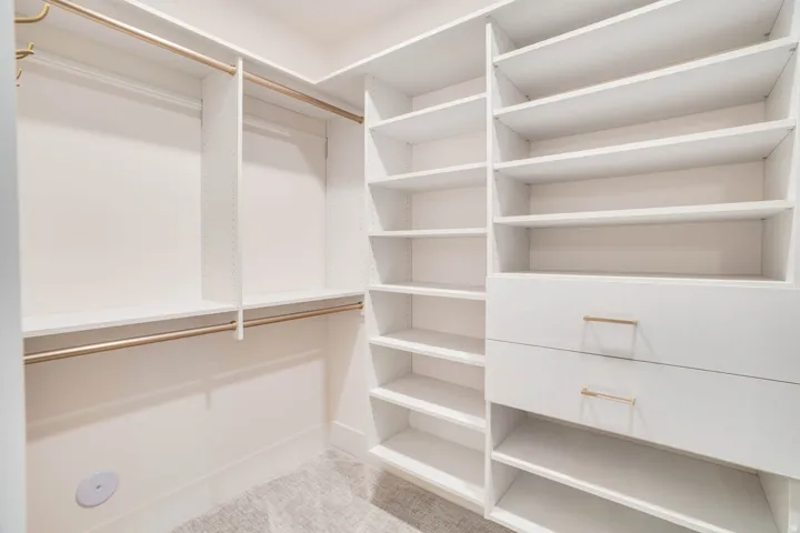 Custom white cabinetry featuring multiple shelving units, two storage drawers with brass-finish hardware, and dual brass-finish hanging rods