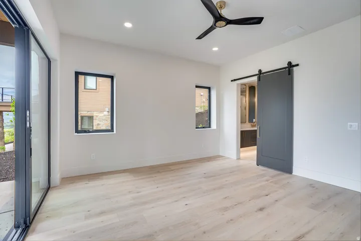 Spacious room featuring light wood-finish flooring, a modern black ceiling fan with brass accents, and recessed lighting