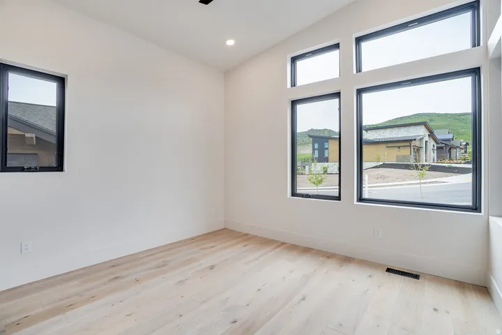 Spacious room featuring light wood-finish flooring, a vaulted ceiling, recessed lighting, and multiple black-framed windows