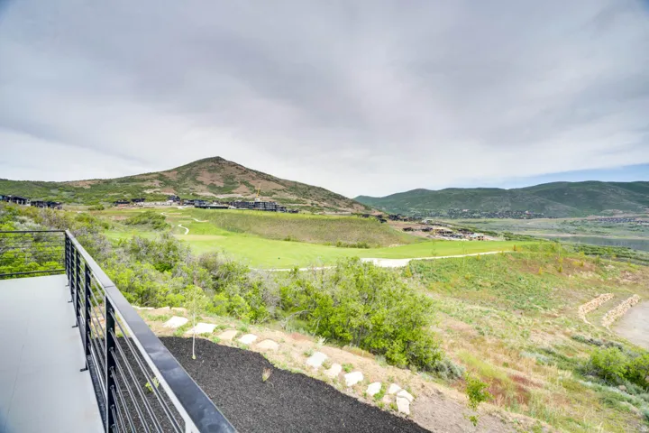 Outdoor deck featuring black horizontal bar railings, overlooking a golf course, distant mountains, and scattered residences