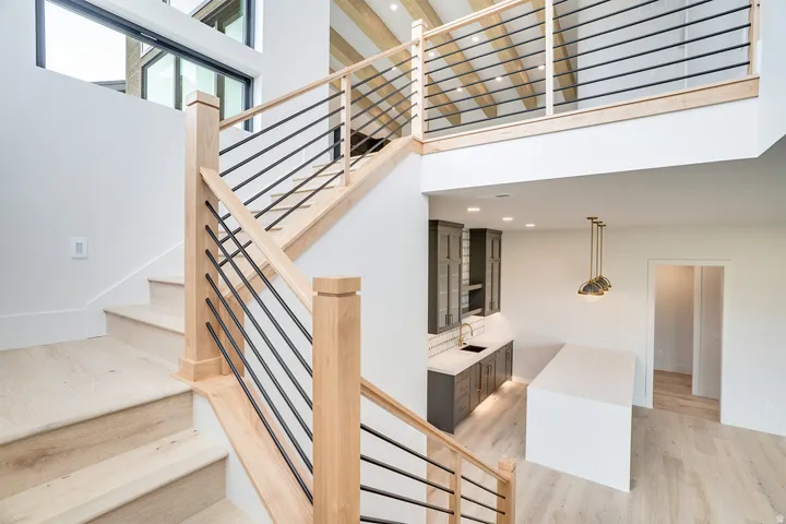 Multi-level interior featuring light wood-finish flooring, a contemporary staircase with natural wood newel posts and black metal balusters, and a loft space with exposed wood beams