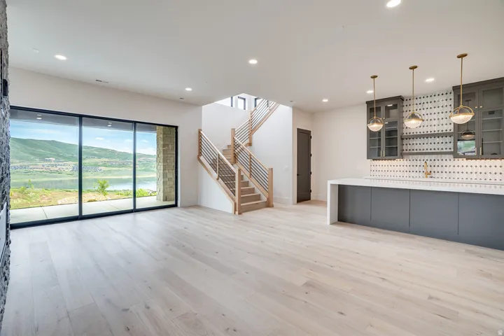 Spacious room featuring wood-finish flooring, a contemporary staircase with metal railings, and a built-in bar with glass-front cabinetry and pendant lighting