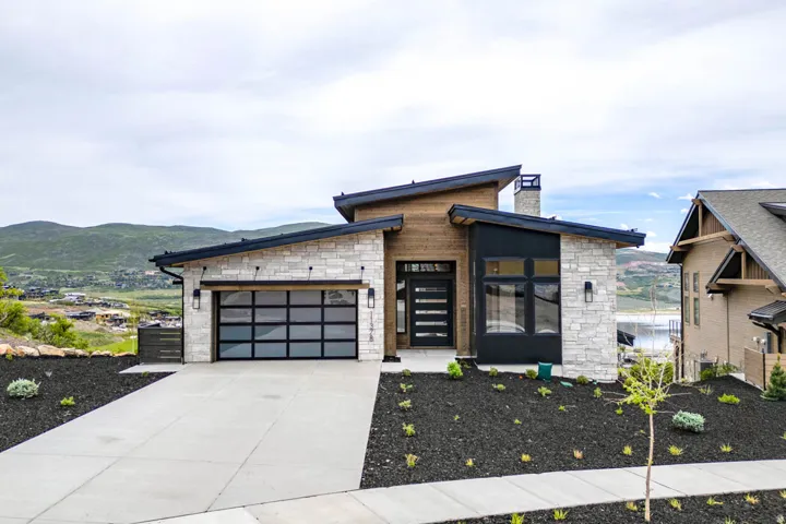 Modern exterior featuring stone veneer, wood paneling, and a black frame garage door with frosted glass panels