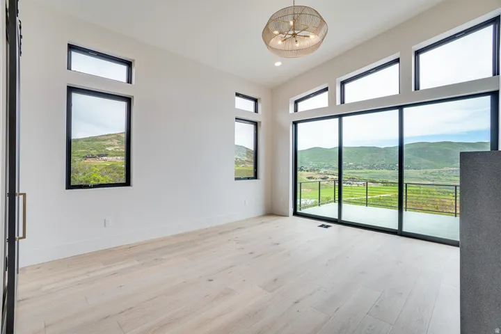 Spacious room featuring vaulted ceilings, light wood-finish flooring, and expansive sliding glass doors opening to a balcony with cable railings
