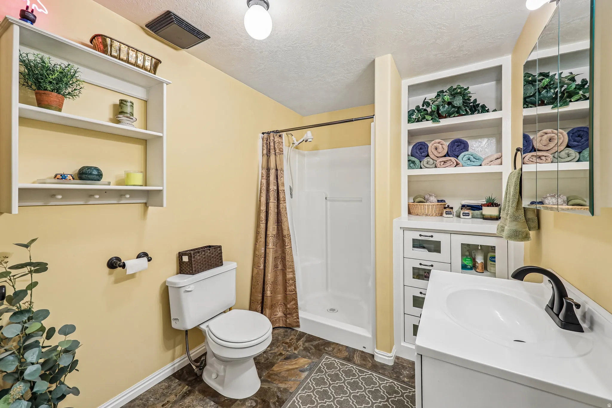 Bathroom featuring a walk-in shower, white vanity with integrated sink, built-in shelving, white wall-mounted shelving unit, and dark-finish flooring