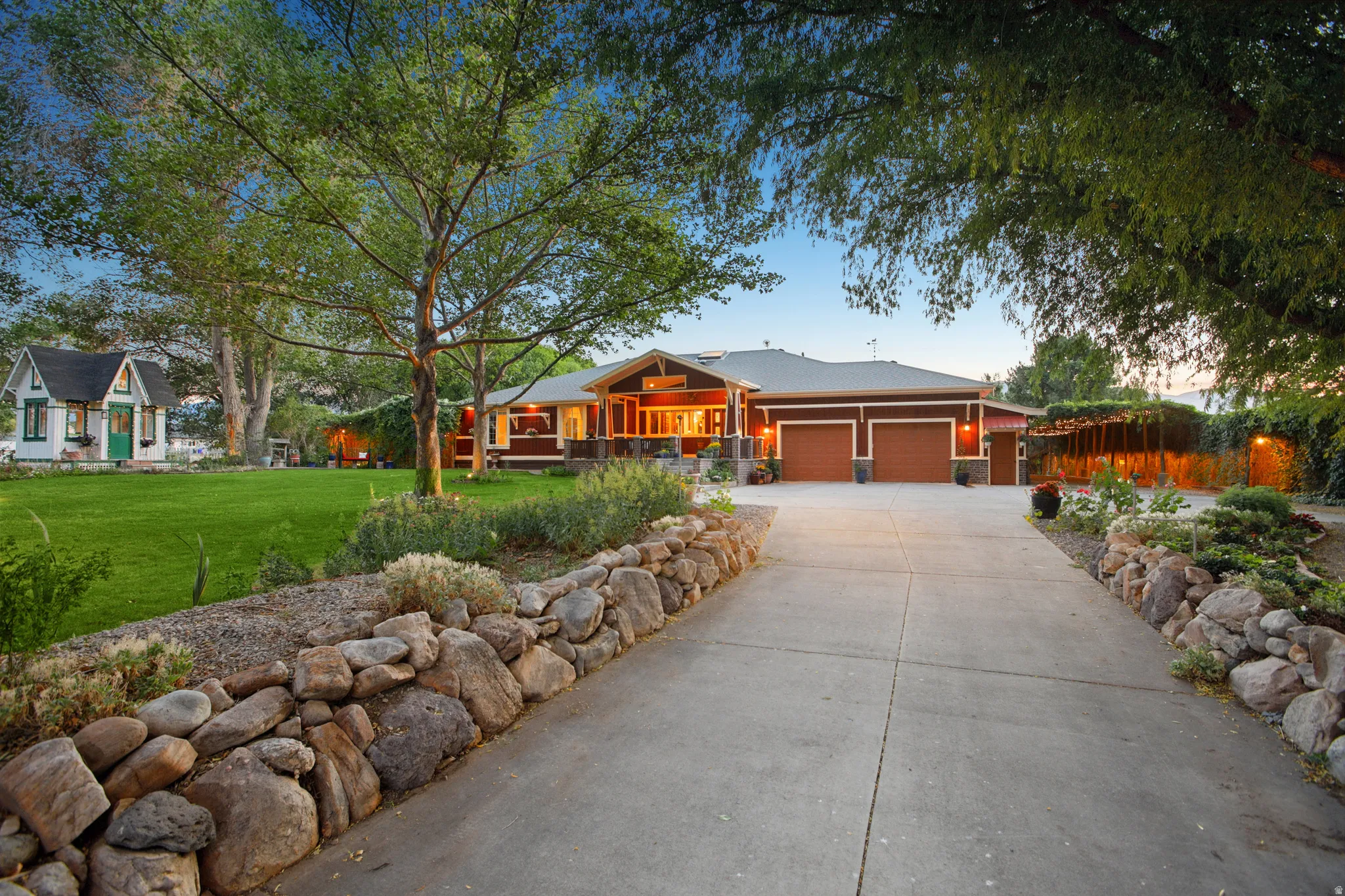 Main residence with red siding and dual garage doors, featuring a concrete driveway bordered by rock landscaping