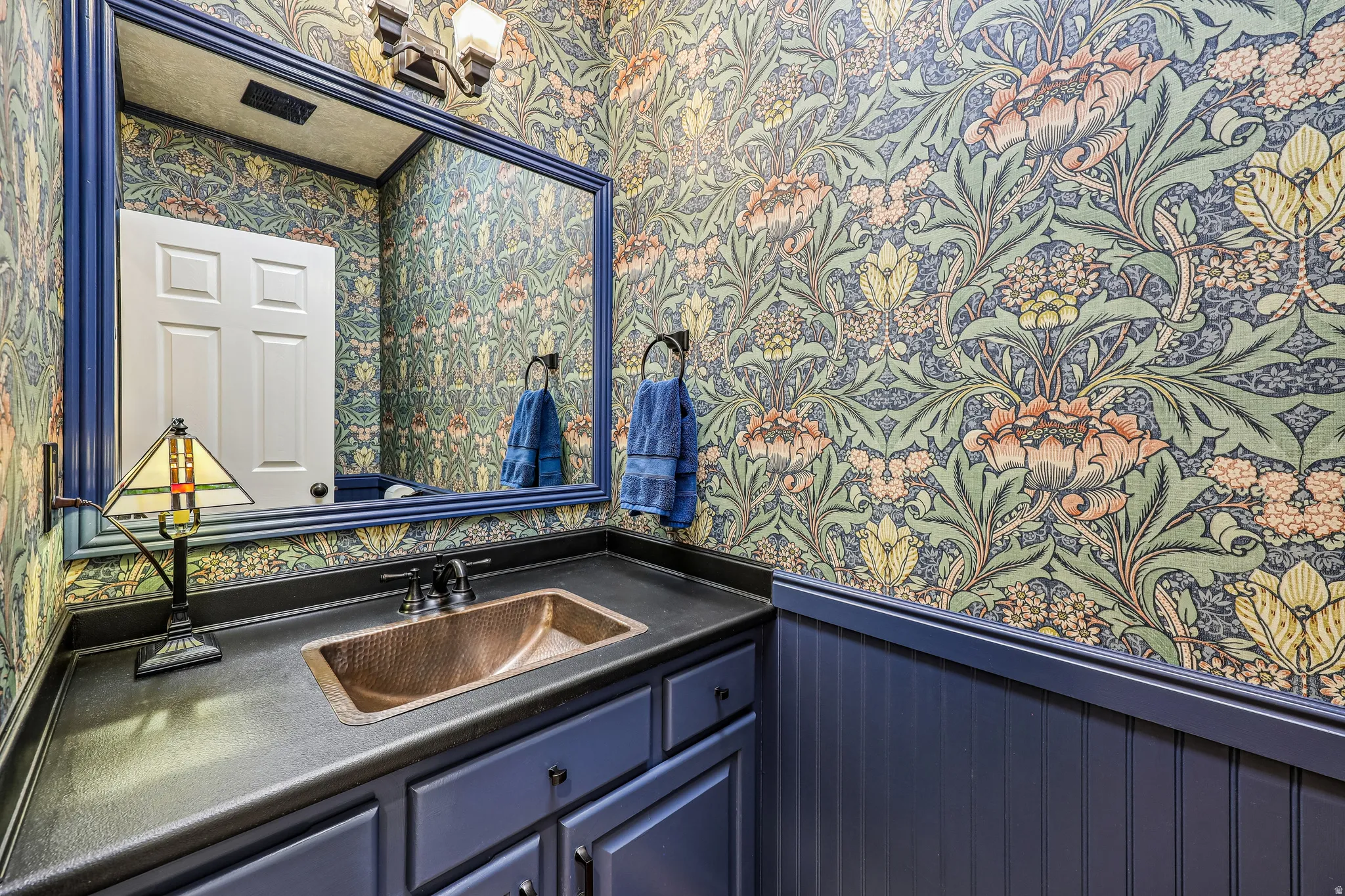 Powder room featuring a copper vessel sink, dark countertop, and custom floral wallpaper