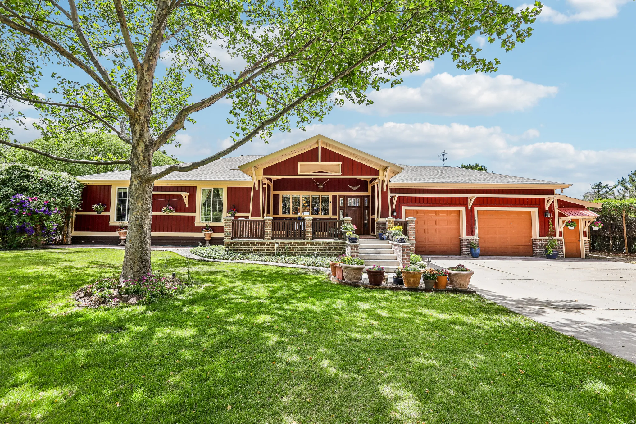 Red exterior siding featuring decorative trim, an inviting front porch, a two-car garage, established landscaping, and a paved driveway