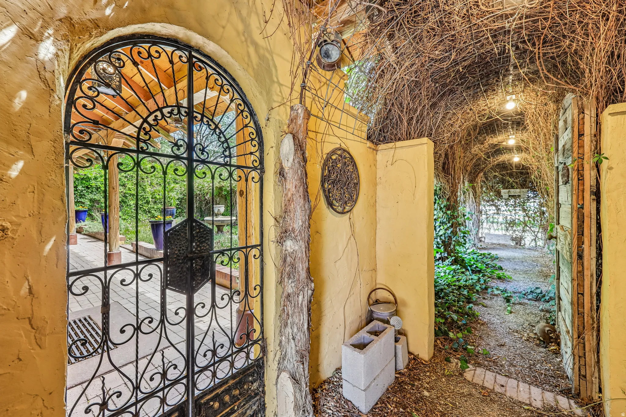 Arched wrought iron gate with intricate scrollwork, opening to an outdoor patio with paver flooring