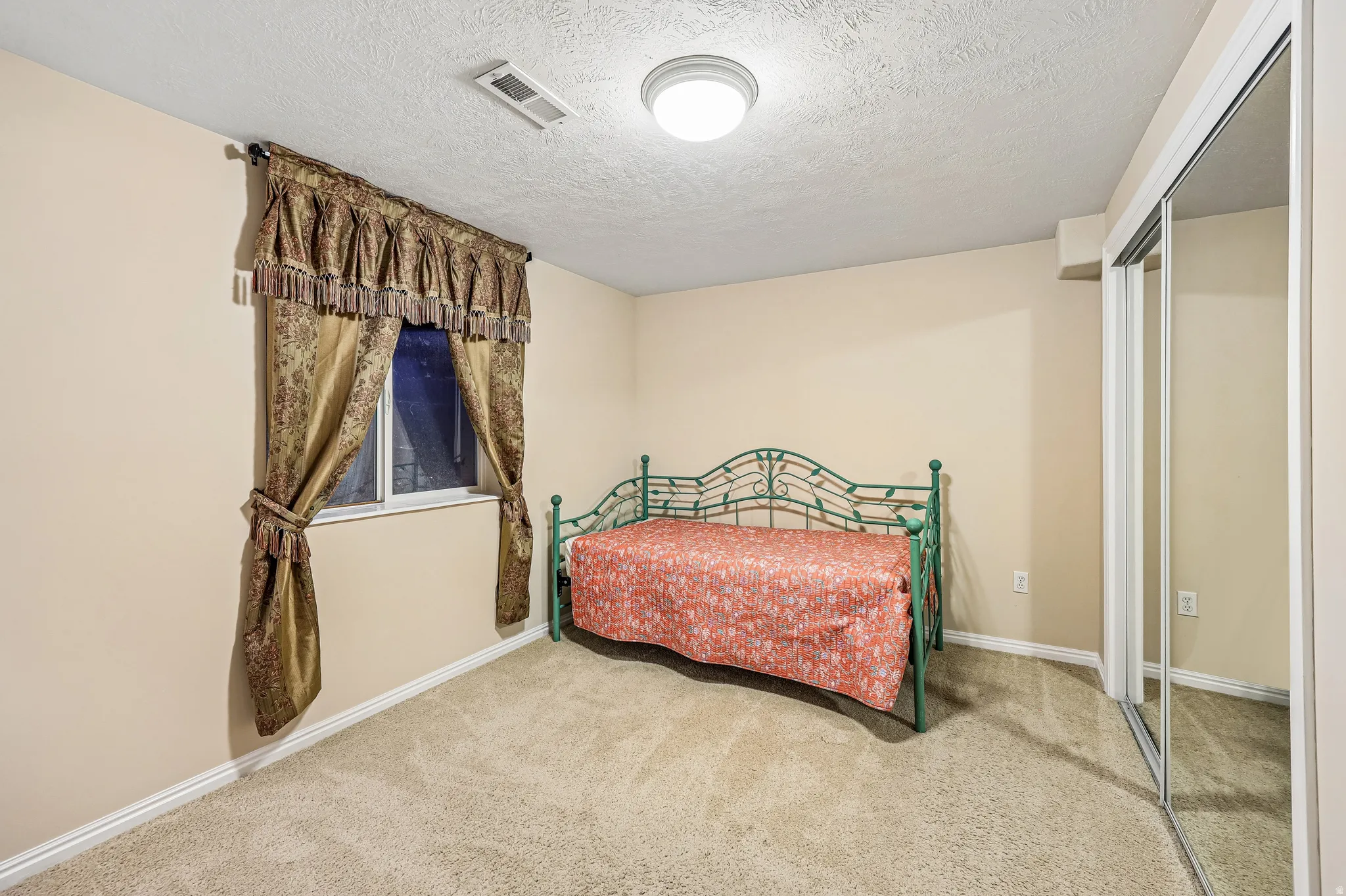 Carpeted room with a window featuring decorative drapes, ceiling-mounted light fixture, and mirrored closet doors