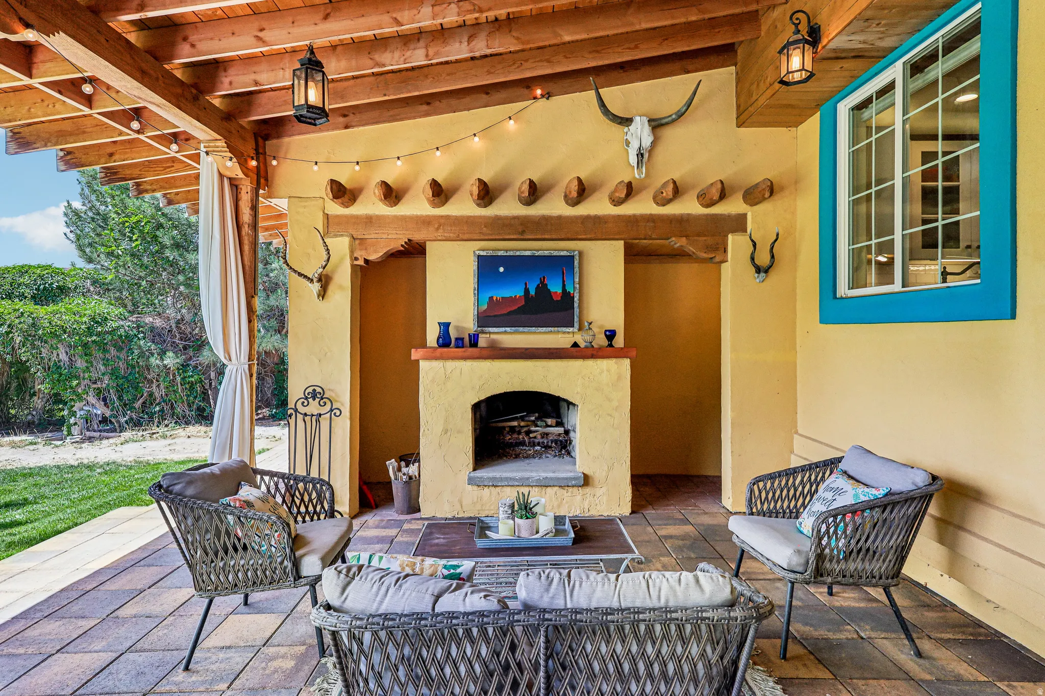 Covered patio featuring an exposed wood beam ceiling, string lighting, and an adobe-style fireplace