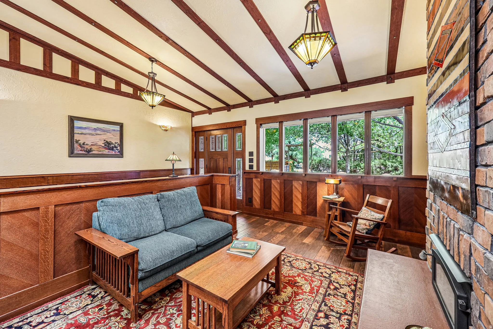 Vaulted ceiling with exposed wood beams, extensive wood paneling, multiple transom windows, wood-finish flooring, and a brick-clad fireplace