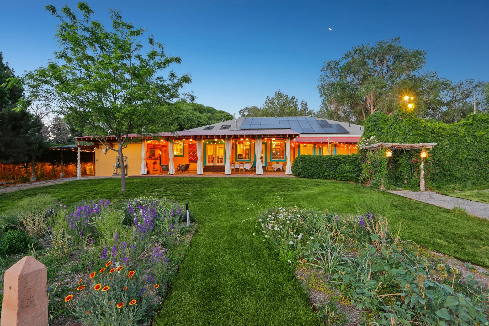 Landscaped front yard with a vibrant flower garden, lush green lawn, and mature trees