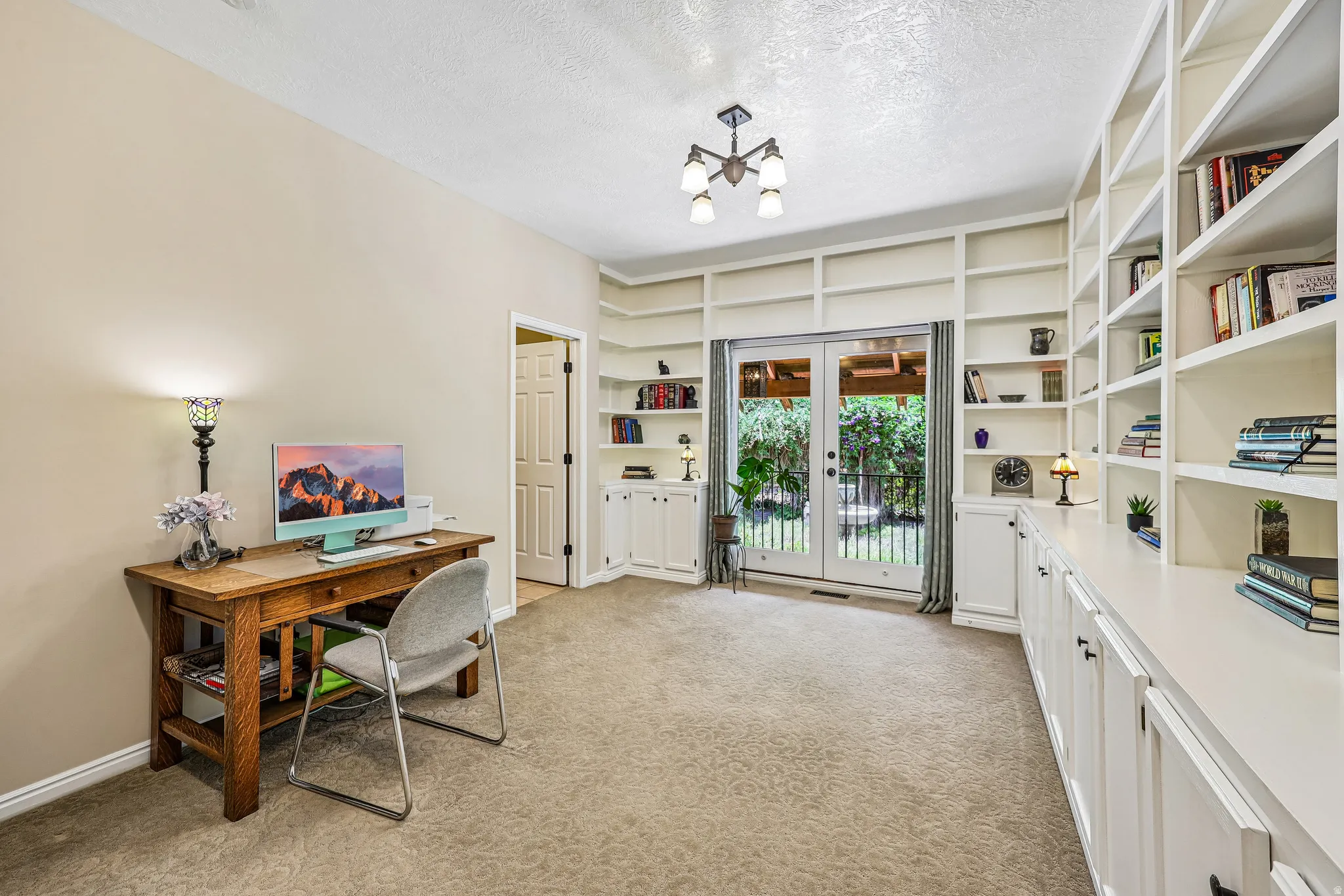 Room featuring extensive built-in shelving, white French doors, and ceiling-mounted lighting fixture