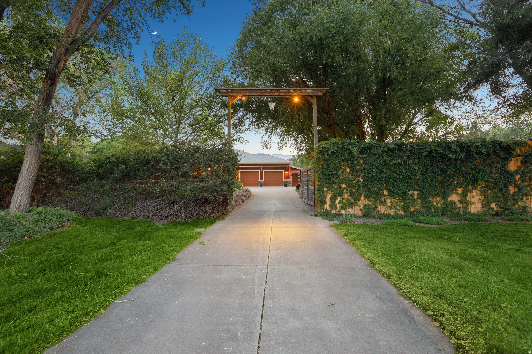 Concrete driveway framed by mature landscaping, leading to a two-car garage with rich brown doors