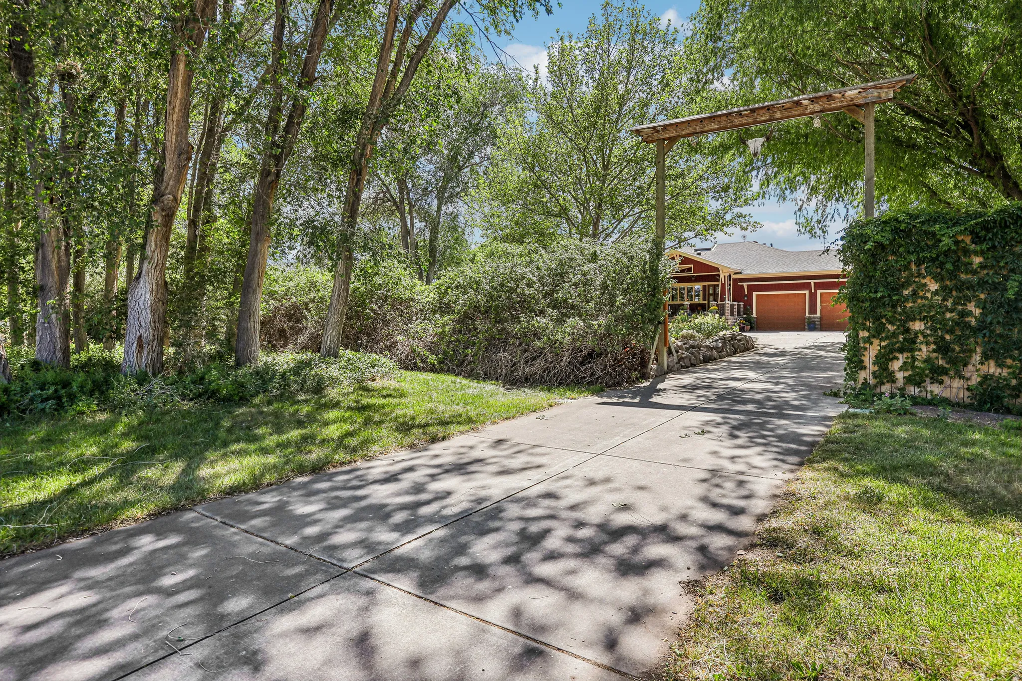 Concrete driveway leading to a red-sided residence with two garage doors and a wooden archway entry