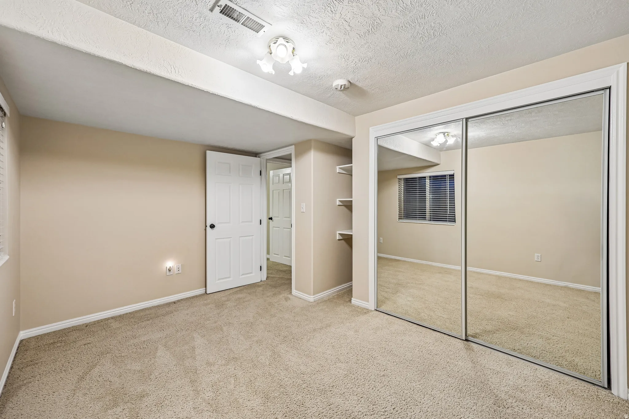 Carpeted interior space featuring neutral tone walls, a mirrored sliding door closet, and built-in shelving