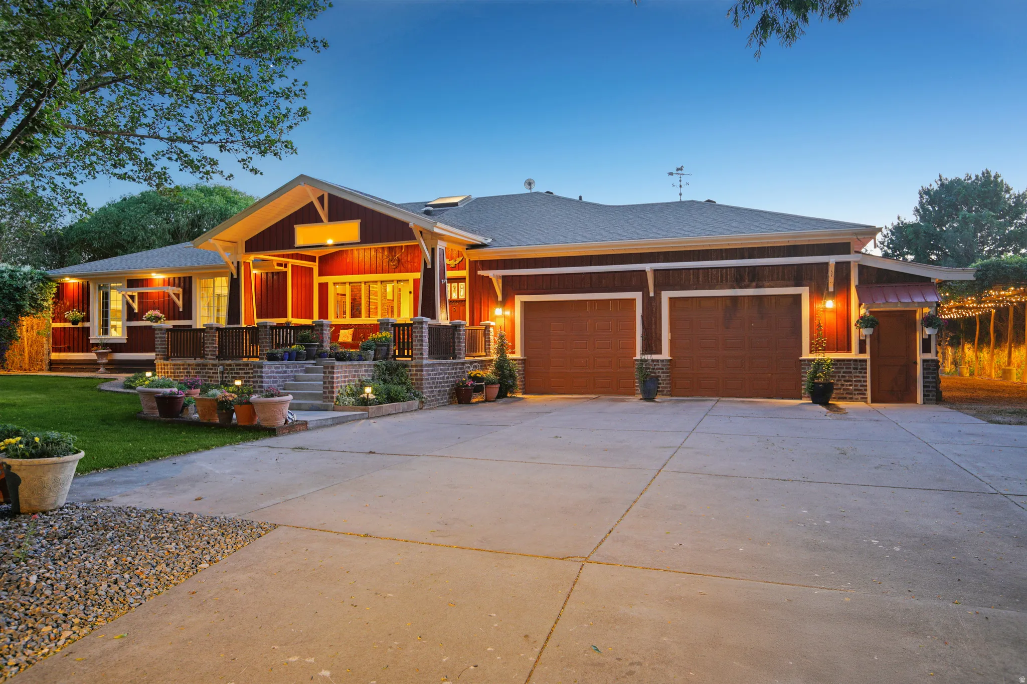 Craftsman-style home featuring red siding, a two-car garage with wood-finish doors, a covered front porch, stone column accents, and a concrete driveway