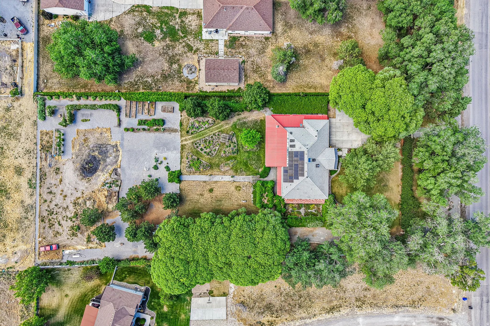 Aerial view showcasing the property's expansive lot with a main residence, dedicated garden area, mature trees, and solar panels