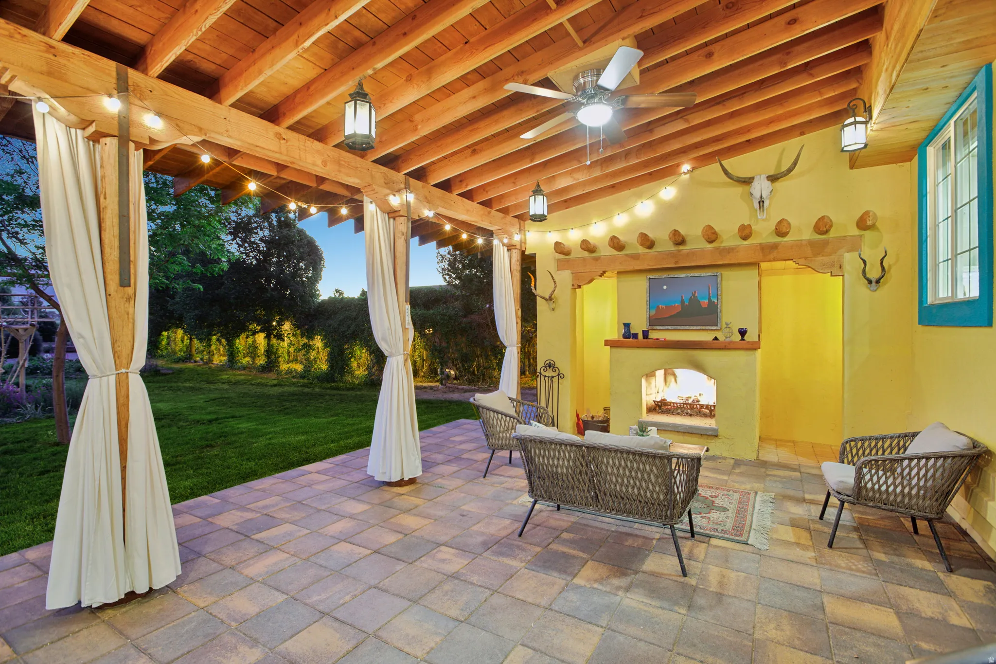 Covered outdoor patio featuring a wood-beam ceiling, ceiling fan, and string lighting