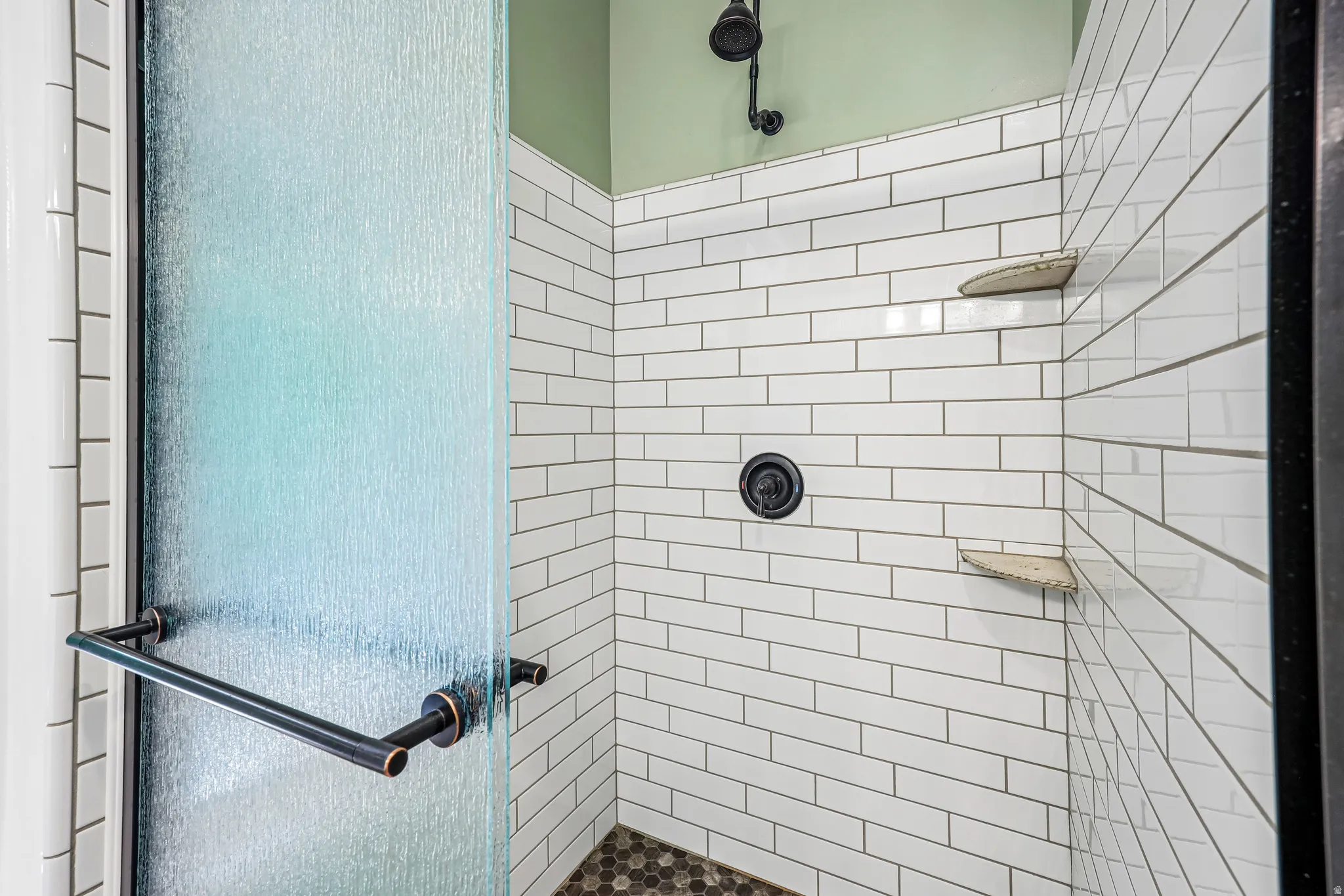 Shower enclosure featuring a textured glass door, matte black hardware, white subway tile walls, a rain showerhead, and two corner shelves