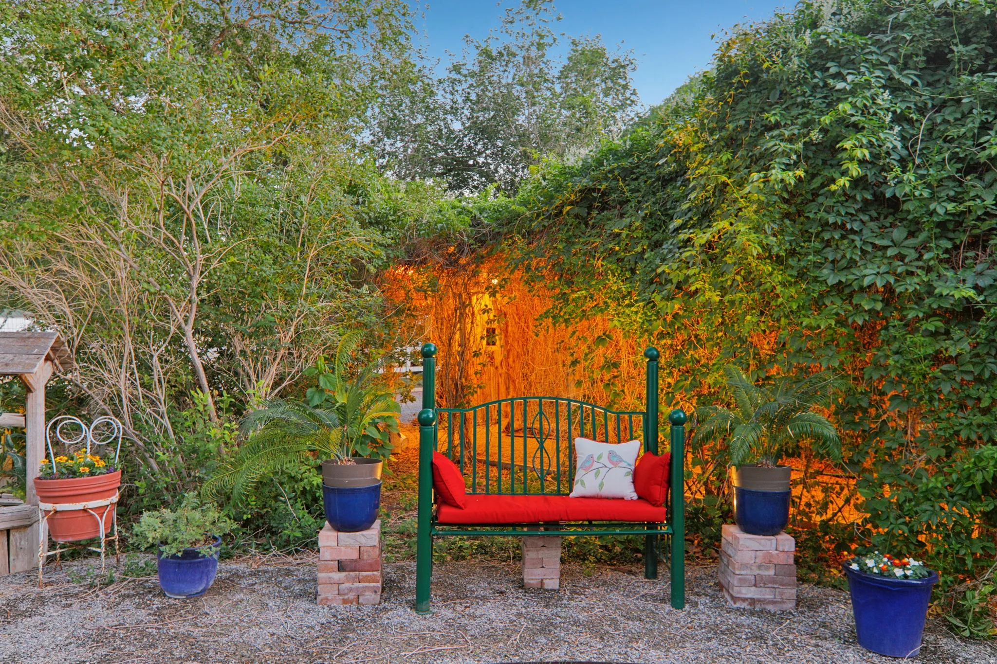 Outdoor seating area featuring a green metal bench with red cushions and a decorative pillow