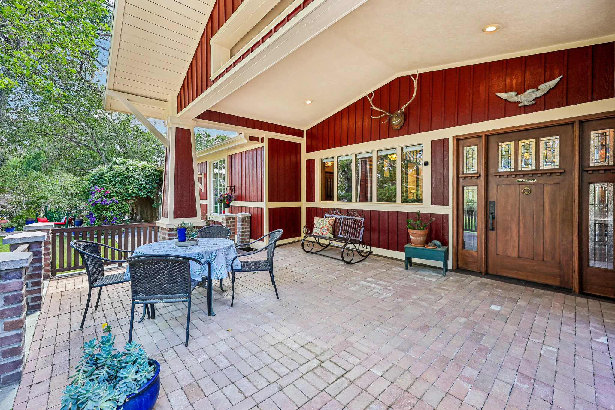 Expansive covered front porch featuring brick paver flooring, a solid wood entry door with decorative glass inserts, and a horizontal wood siding exterior
