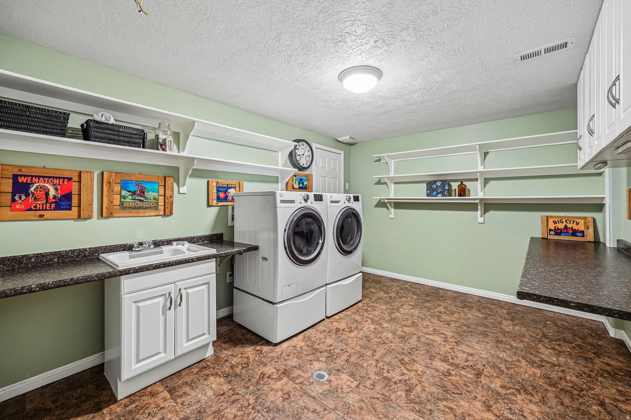 Spacious utility room featuring extensive wall shelving, white cabinetry, a utility sink, and ample countertop space