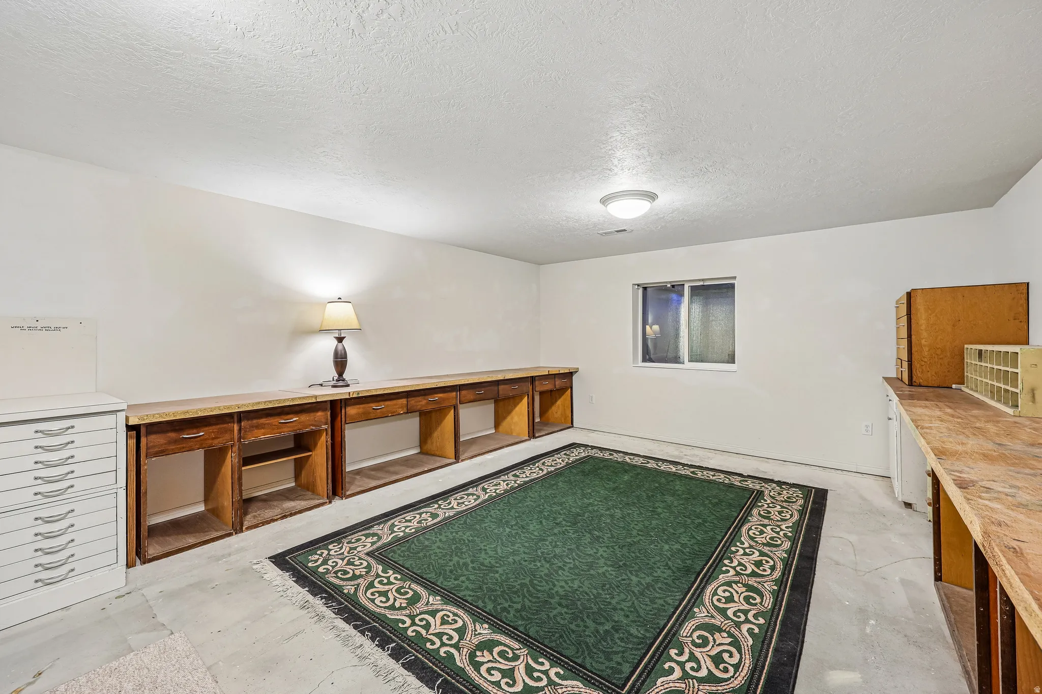 Spacious room featuring extensive built-in wooden workbenches with laminate countertops, a single casement window, and a flush-mount ceiling light fixture