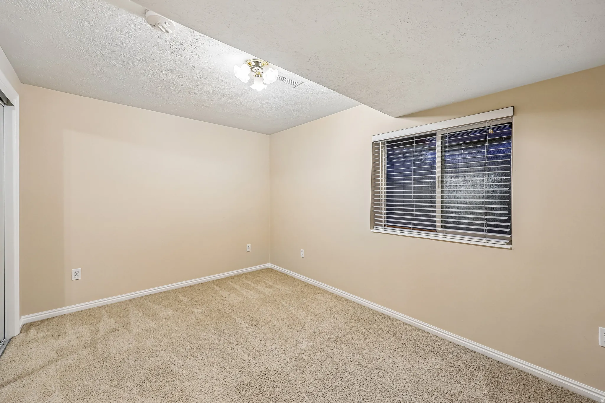Carpeted room featuring a window with horizontal blinds, light beige walls, and white trim