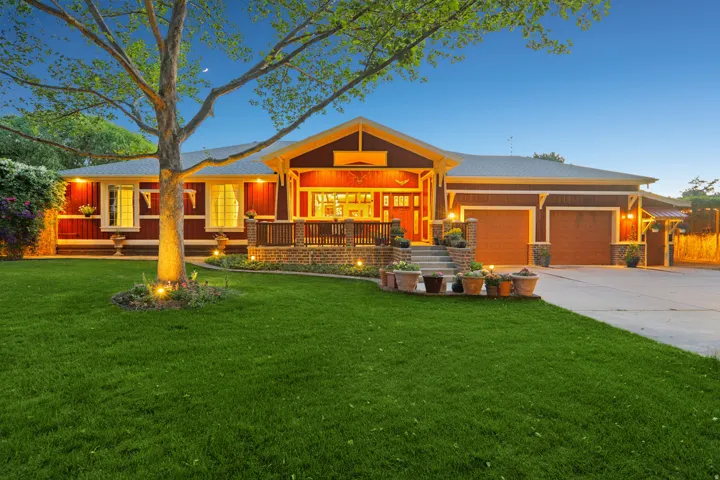 Craftsman-style home featuring rich red siding, a covered front porch with brick accents, and a dual-bay garage