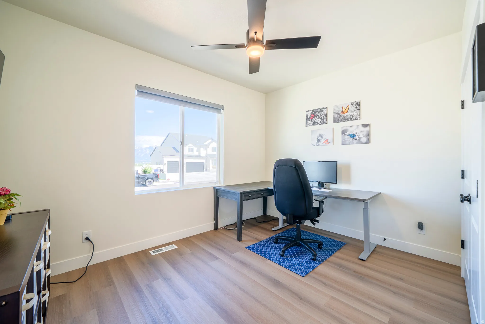Room featuring light wood-finish flooring, a large window with roller shades, and a ceiling fan with integrated lighting