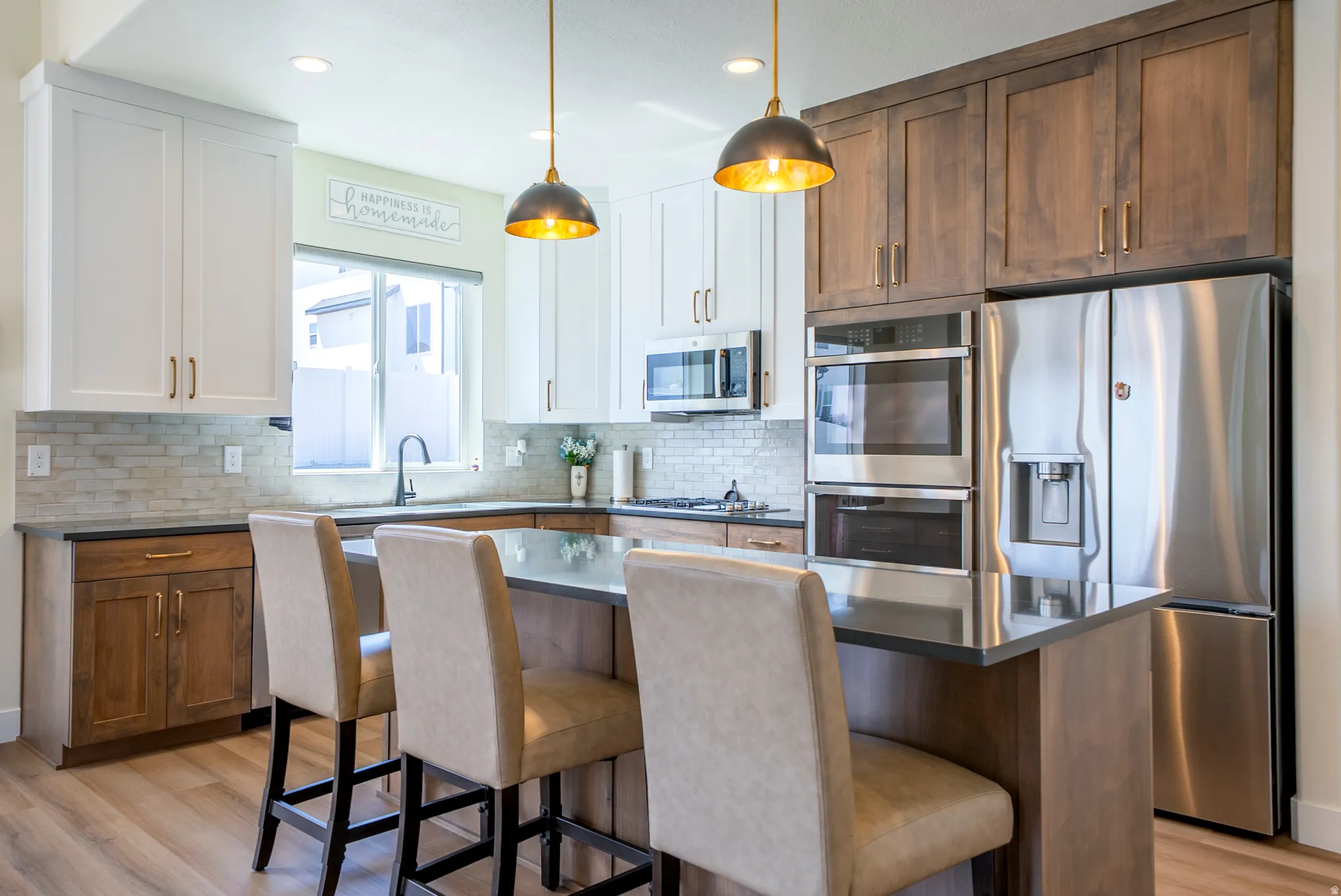 Modern kitchen featuring a central island with bar seating, dual-tone cabinetry, stainless steel appliances, and wood-finish flooring