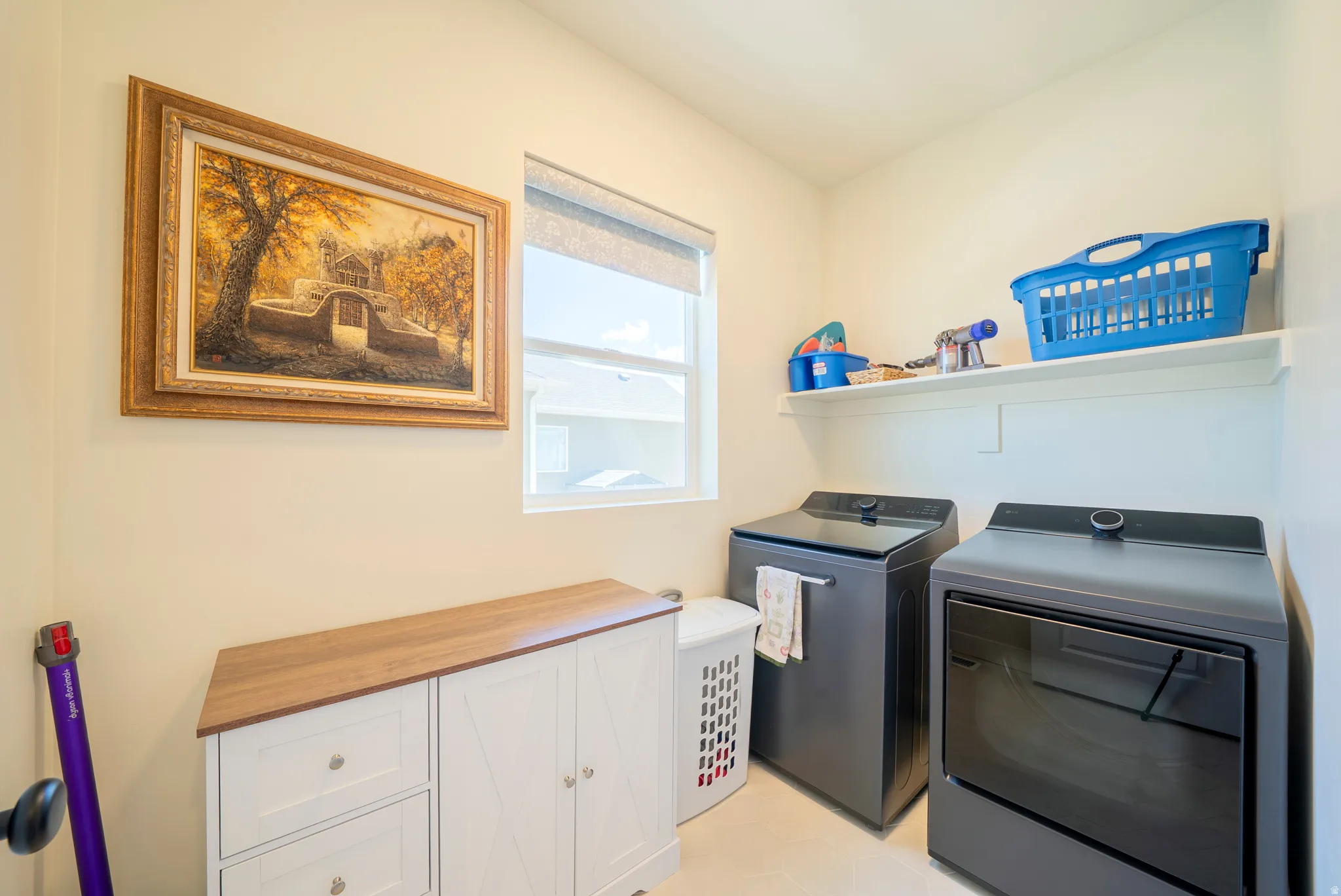 Dedicated laundry space featuring a window, built-in shelving, and a wood-finish countertop cabinet with white cabinetry