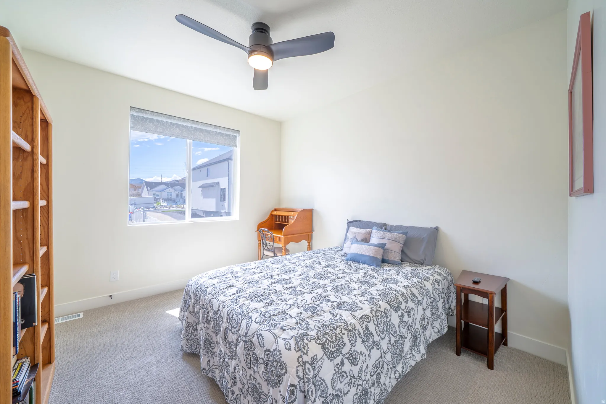 Bright room featuring a large window with roller shades, light-colored walls, and neutral carpeting