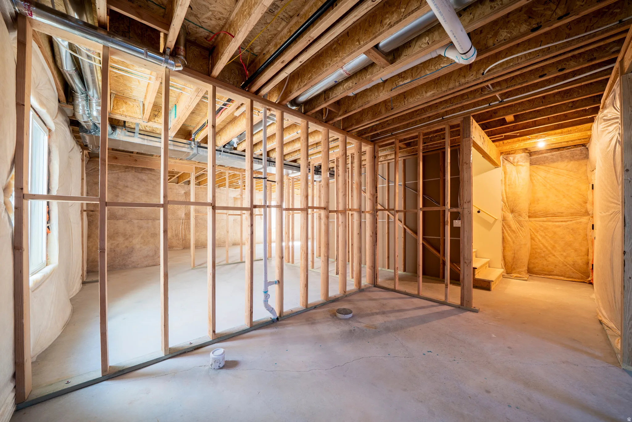 Expansive unfinished basement featuring visible wood framing, concrete flooring, exposed ceiling joists, and a window for natural illumination
