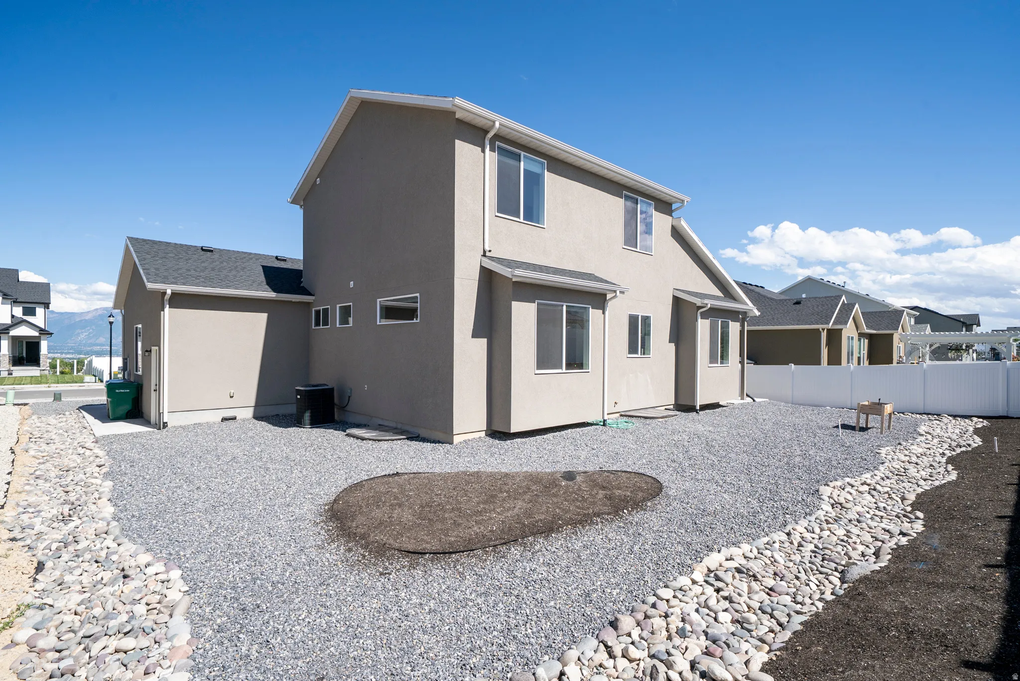Expansive backyard featuring gravel landscaping, a white privacy fence, and a decorative rock border