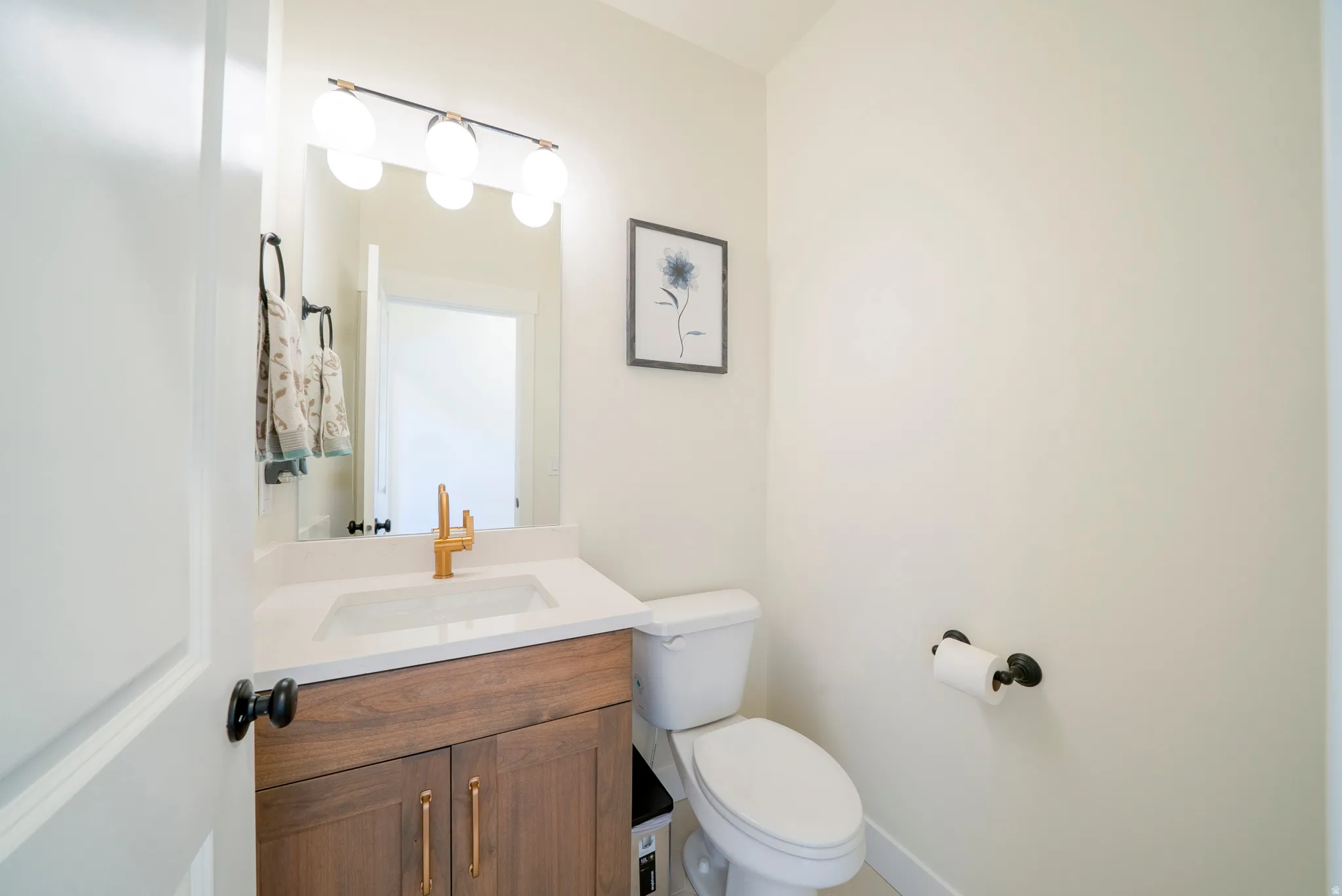 Powder room featuring a wood-finish vanity with gold-tone hardware, a white countertop, and an integrated rectangular sink with a gold-tone faucet