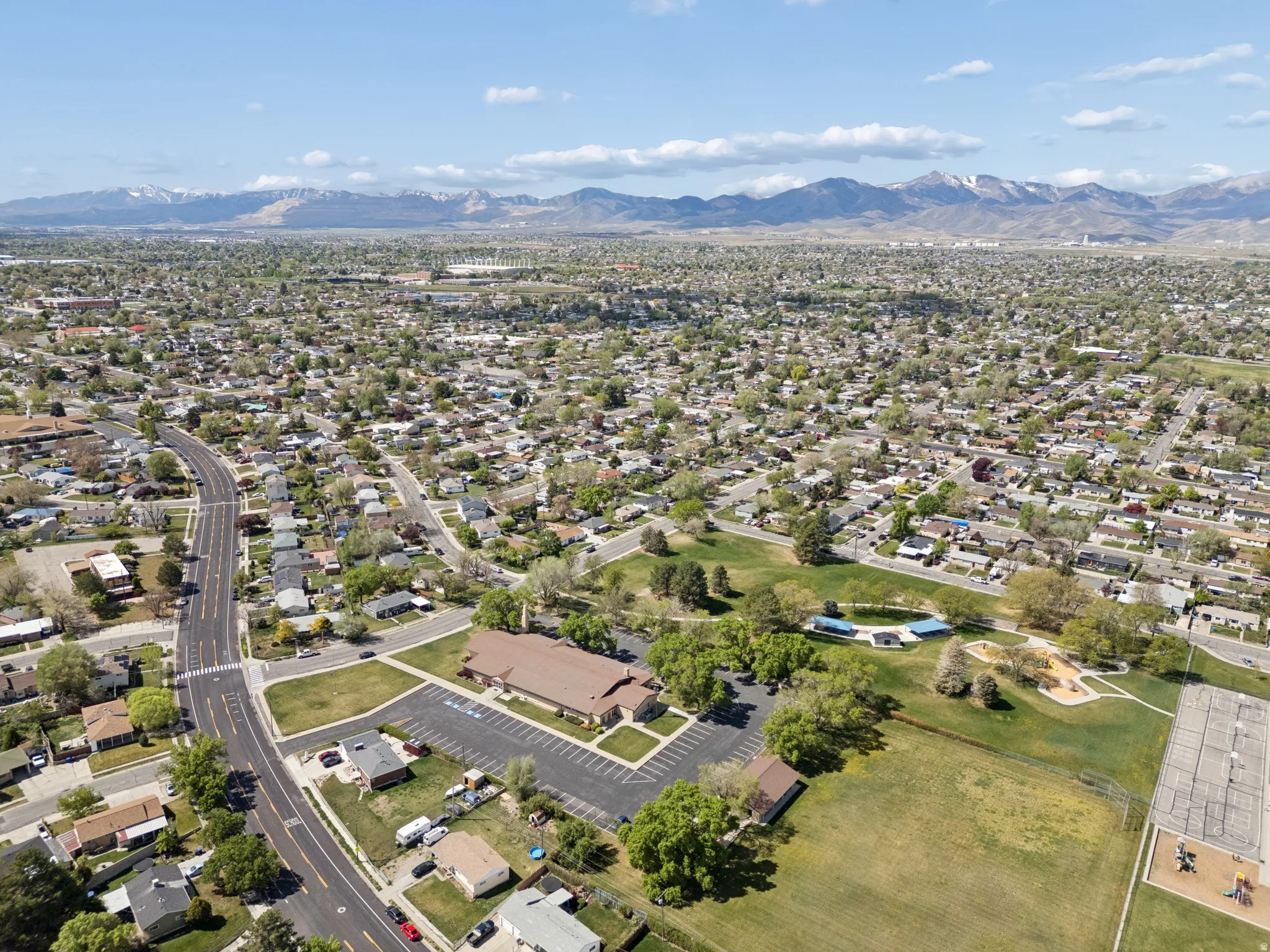 Expansive aerial encompassing a residential area with varied housing, green spaces, and a prominent mountain range in the distance.