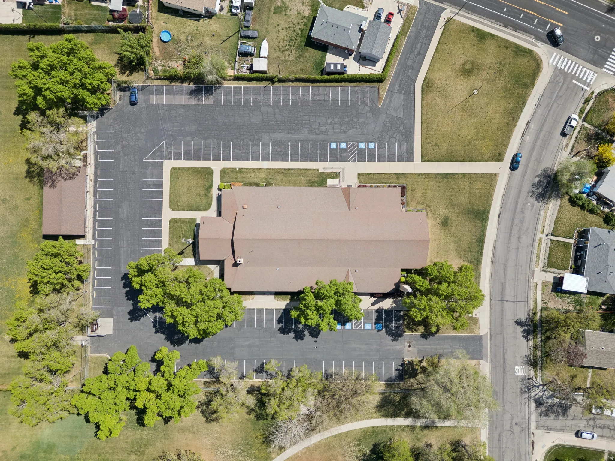 Expansive commercial property featuring a large building with a brown shingle roof, extensive paved parking areas, and mature surrounding trees.