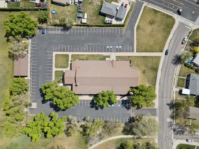 Expansive commercial property featuring a large building with a brown shingle roof, extensive paved parking areas, and mature surrounding trees.
