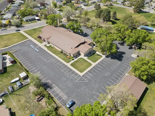 Large commercial building with a brown shingle roof, extensive paved parking areas, and mature surrounding trees.