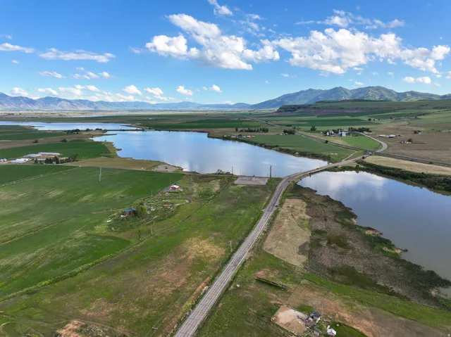 Expansive agricultural landscape featuring a large body of water, a bridge crossing the water, and distant mountains under a blue sky with white clouds