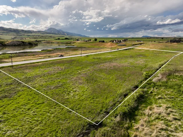 Expansive green lot featuring a paved road frontage, natural water body, distant mountains, and varied topography