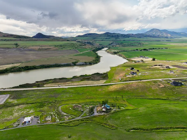 Expansive green landscape featuring a prominent river, distant mountains, a residential property, and a paved road