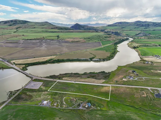 Expansive land parcel featuring direct road frontage, a partially green landscape, and proximity to a body of water with distant mountainous terrain