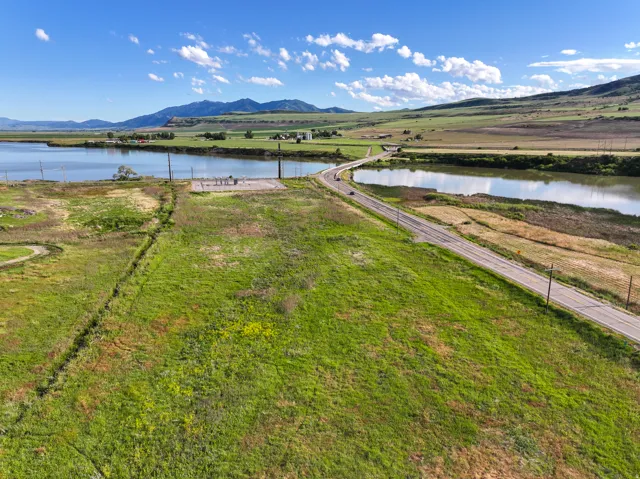 Expansive green terrain bordering a body of water, with a paved roadway and a distant bridge