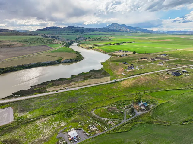 Riverfront property with expansive green fields, distant mountains, and a scenic roadway